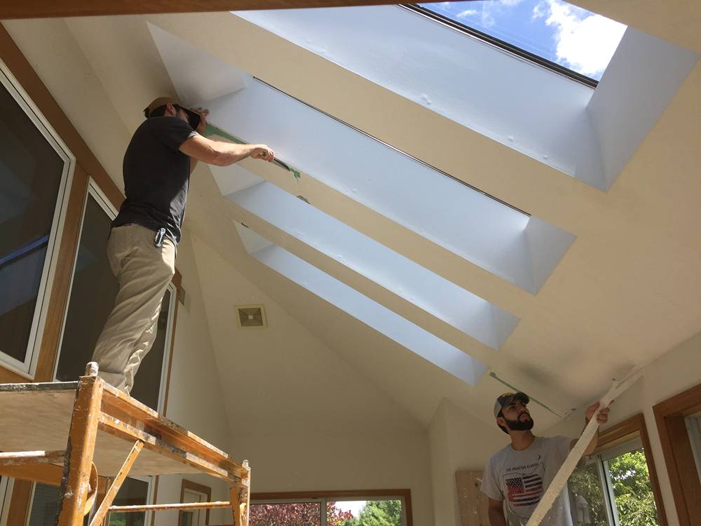 Technician repairing drywall near skylights on scaffolding in a Columbus home