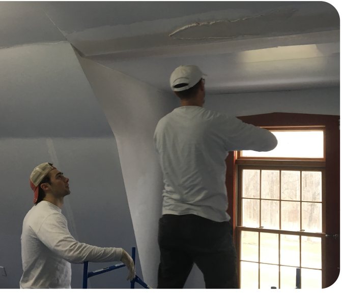 Two drywall repair specialists fixing HVAC-related condensation damage on a ceiling, preparing surface for texture blending.