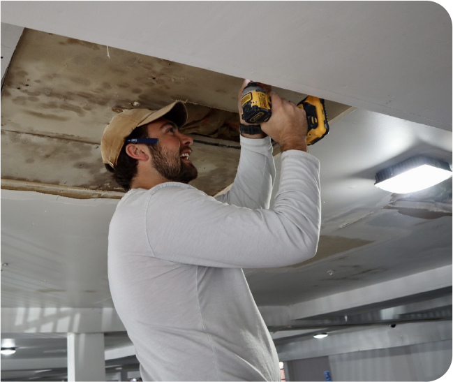 Drywall professional securing ceiling panel to repair large HVAC moisture damage access opening in a commercial area.