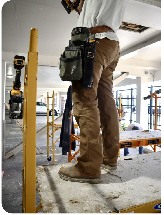 Drywall contractor working from scaffolding performing commercial drywall repairs inside a business property.