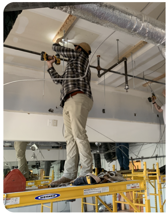 Construction crew installing drywall and ceiling infrastructure during commercial remodeling project using scaffolding.