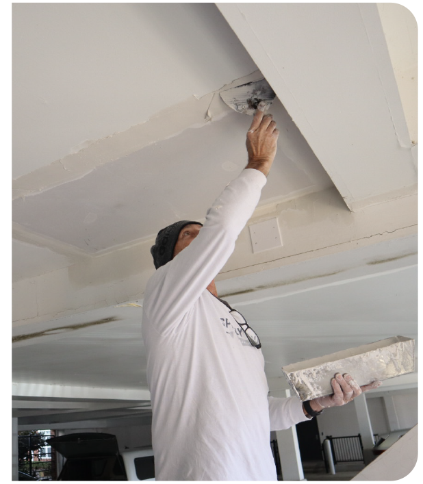 Professional drywall technician applying compound to patch a ceiling seam for smooth drywall repair and finishing.
